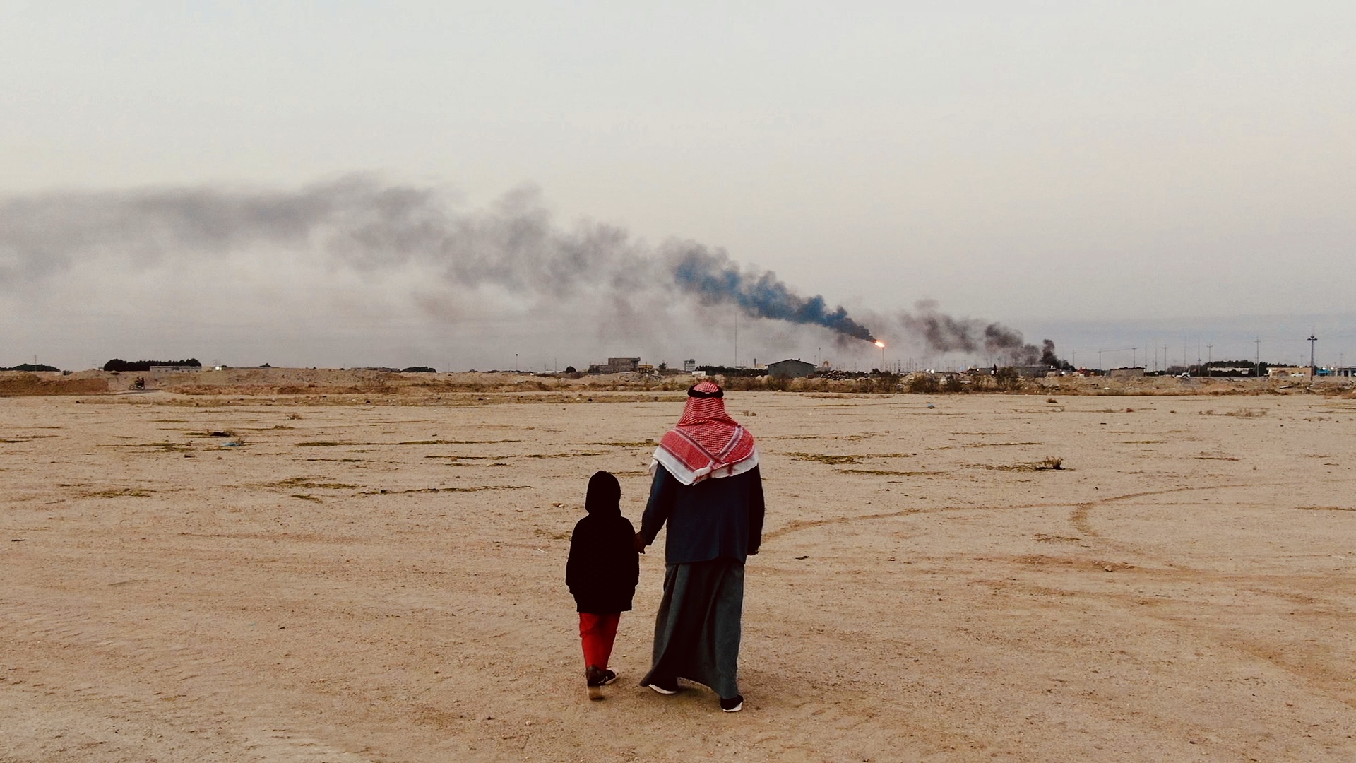 Fatima’s father, Hasan, holding hands with one of his daughters, looks out at flare stacks near his family’s home.